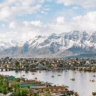 Panoramic view of Srinagar with Dal Lake, traditional houseboats, shikaras, and snow-capped Himalayan mountains in the background.